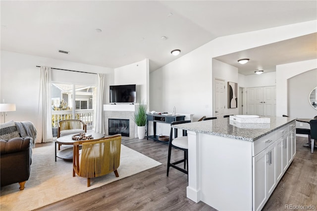 kitchen with a tiled fireplace, wood-type flooring, light stone countertops, and white cabinets