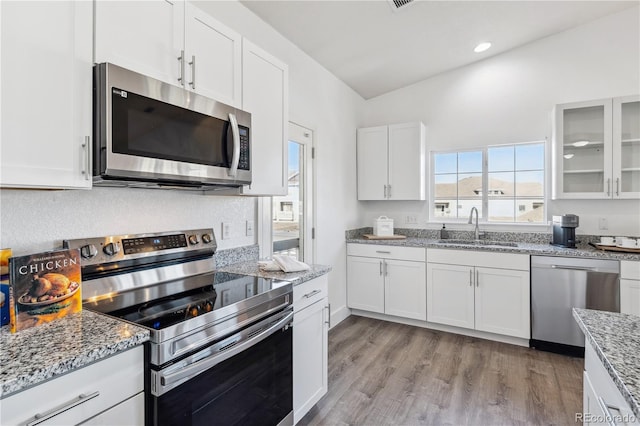 kitchen with appliances with stainless steel finishes, sink, white cabinets, light stone counters, and light hardwood / wood-style flooring