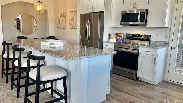 9471 Ashbury Cir Unit 202, Parker, CO 80134 - kitchen with stainless steel appliances, light wood-type flooring, a center island, a kitchen bar, and white cabinets