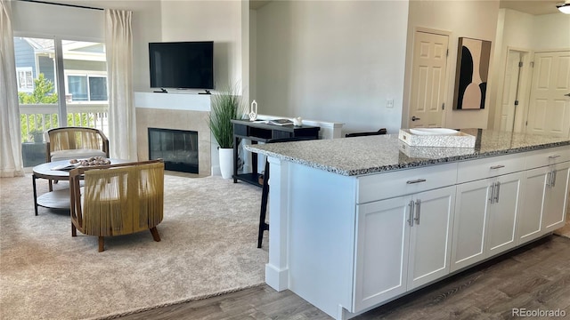 9471 Ashbury Cir Unit 202, Parker, CO 80134 - kitchen featuring dark wood finished floors, white cabinets, light stone countertops, a fireplace, and a center island