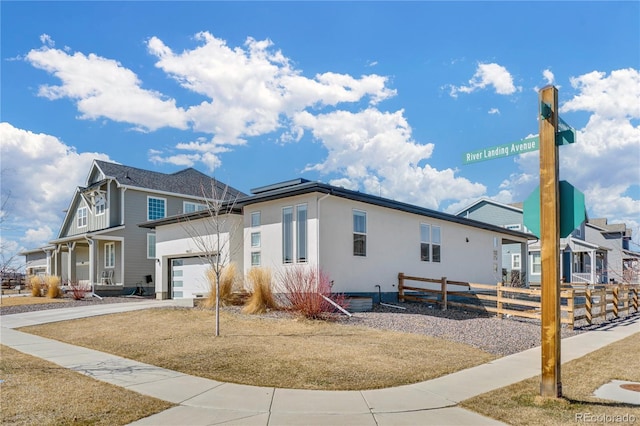 view of side of home with fence, a residential view, concrete driveway, stucco siding, and an attached garage