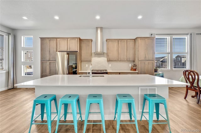 kitchen featuring a sink, a kitchen breakfast bar, smart refrigerator, and wall chimney exhaust hood