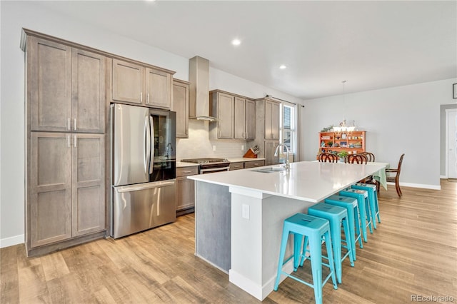 kitchen featuring light wood-style floors, appliances with stainless steel finishes, a sink, and wall chimney exhaust hood