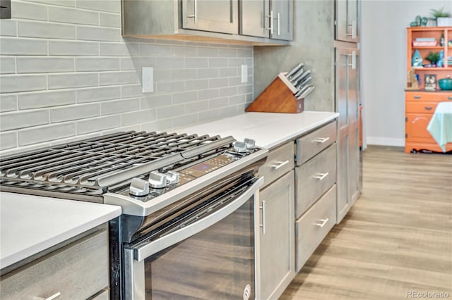 kitchen featuring light wood finished floors, gas stove, light countertops, decorative backsplash, and baseboards