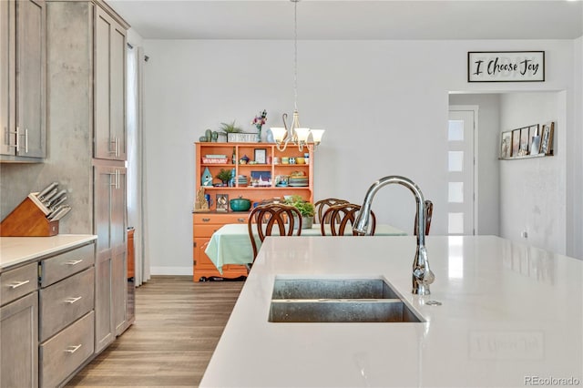 kitchen with light countertops, wood finished floors, a sink, gray cabinetry, and a chandelier