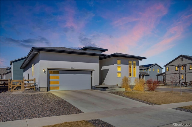 view of front facade featuring stucco siding, driveway, fence, and a garage
