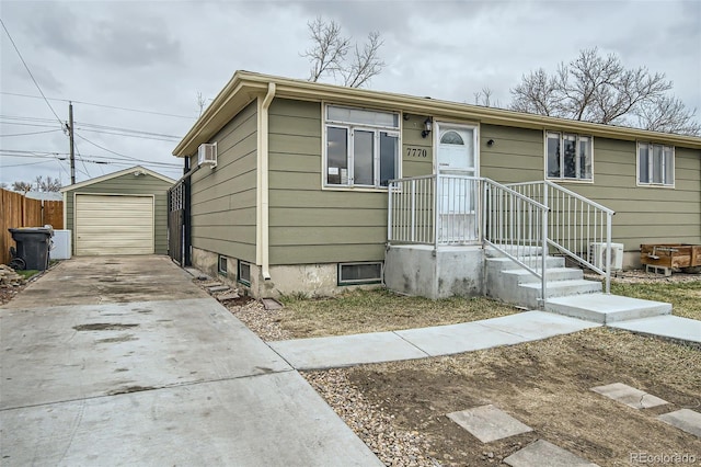 view of front facade featuring a detached garage, fence, concrete driveway, a wall unit AC, and an outbuilding