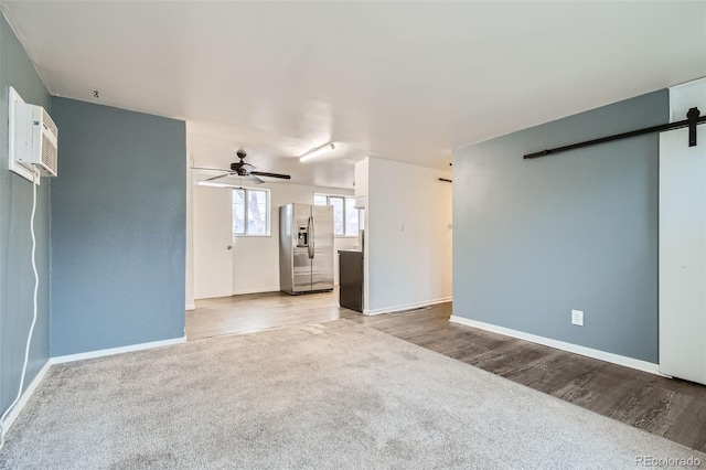 unfurnished living room with ceiling fan, baseboards, a barn door, carpet flooring, and wood finished floors