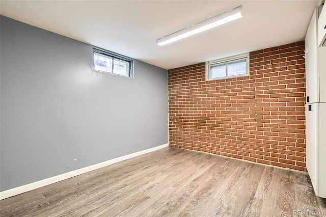 basement with baseboards, wood finished floors, and brick wall