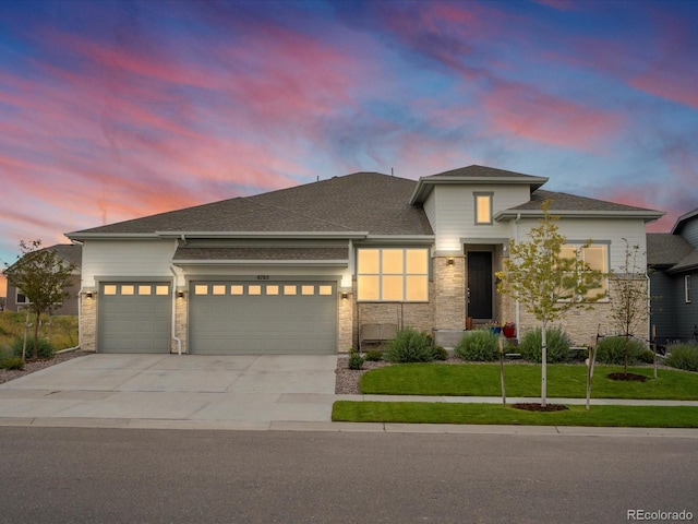 prairie-style home with a garage, stone siding, concrete driveway, and a yard