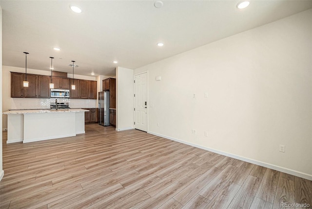 kitchen featuring stainless steel appliances, a center island with sink, pendant lighting, light stone counters, and light hardwood / wood-style floors