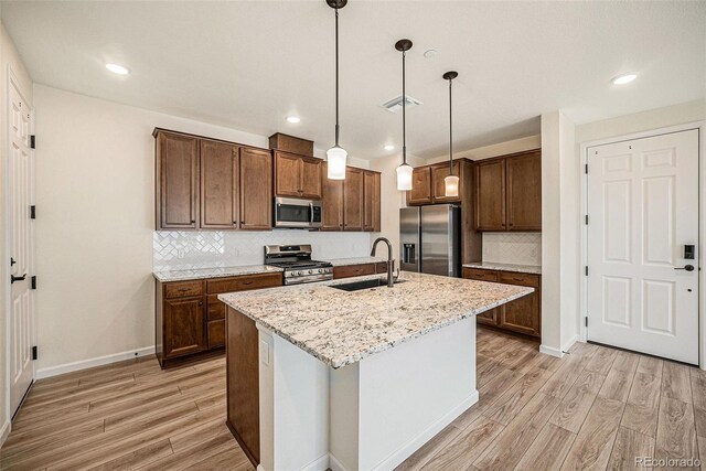 kitchen featuring a kitchen island with sink, light hardwood / wood-style flooring, hanging light fixtures, sink, and appliances with stainless steel finishes