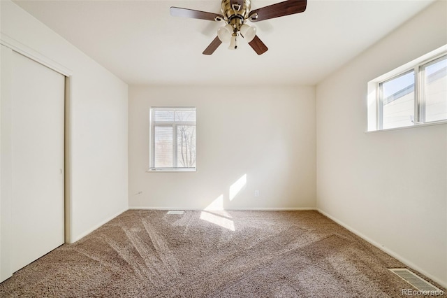 carpeted spare room with a healthy amount of sunlight, visible vents, and ceiling fan