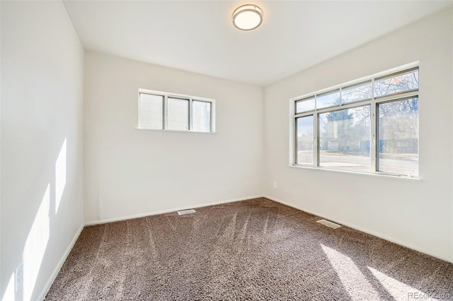 empty room featuring carpet floors, visible vents, plenty of natural light, and baseboards