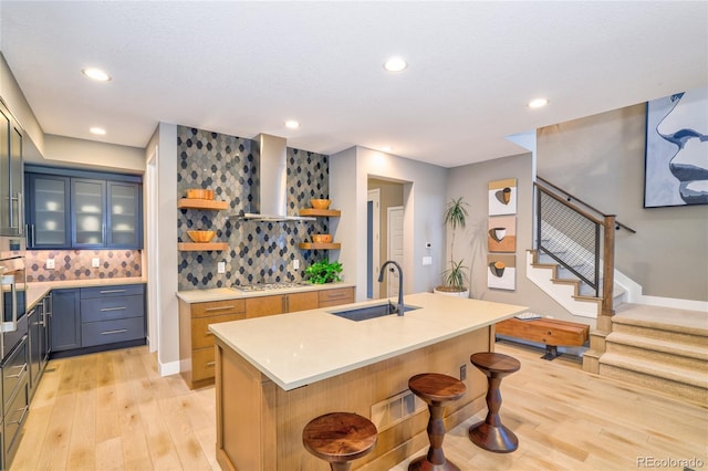 kitchen with sink, wall chimney range hood, an island with sink, decorative backsplash, and appliances with stainless steel finishes