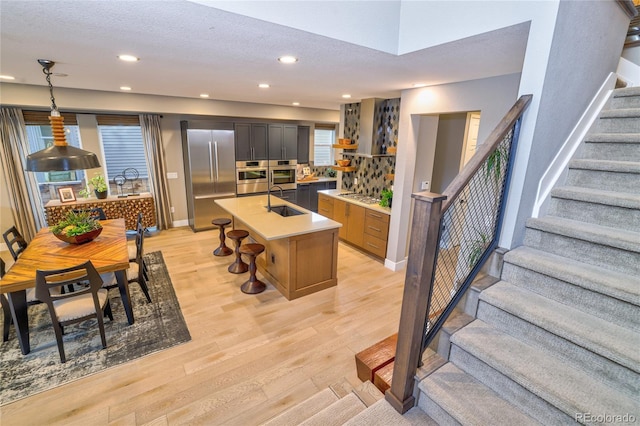 kitchen featuring a center island with sink, hanging light fixtures, light wood-type flooring, a textured ceiling, and stainless steel appliances