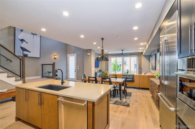 kitchen featuring sink, an island with sink, appliances with stainless steel finishes, decorative light fixtures, and light hardwood / wood-style floors