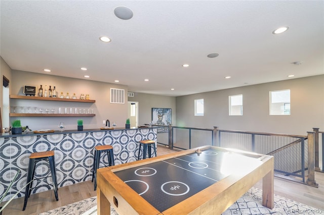 rec room featuring light wood-type flooring, a textured ceiling, and indoor bar