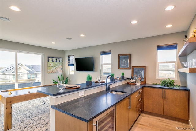 kitchen with kitchen peninsula, beverage cooler, a healthy amount of sunlight, sink, and light hardwood / wood-style flooring