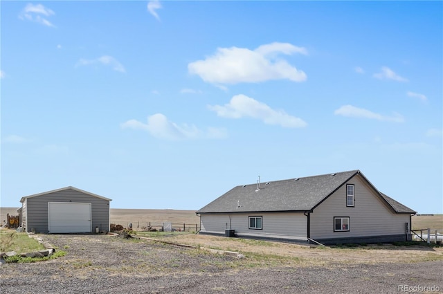 view of side of home with an outbuilding, roof with shingles, fence, a garage, and driveway