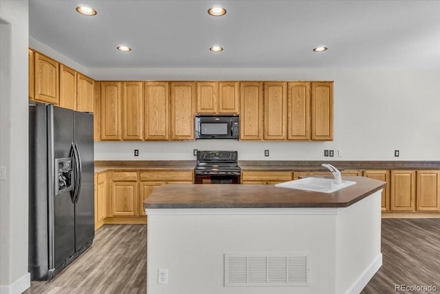 2142 Paint Pony Cir, Castle Rock, CO 80108 - kitchen with black appliances, light wood-type flooring, recessed lighting, dark countertops, and a center island with sink