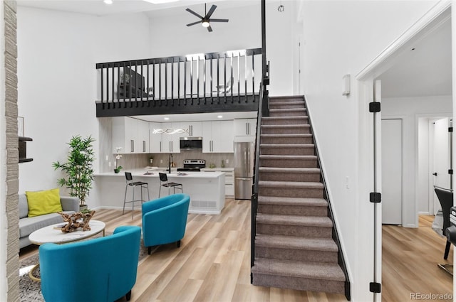 staircase with ceiling fan, sink, hardwood / wood-style floors, and a high ceiling