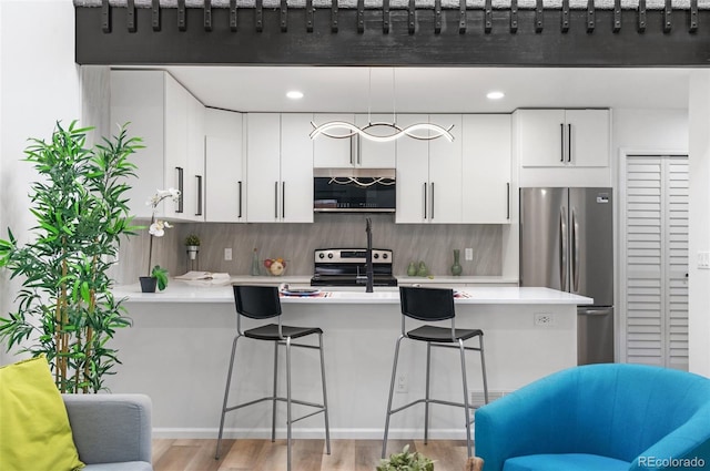 kitchen with appliances with stainless steel finishes, a kitchen breakfast bar, kitchen peninsula, and white cabinets