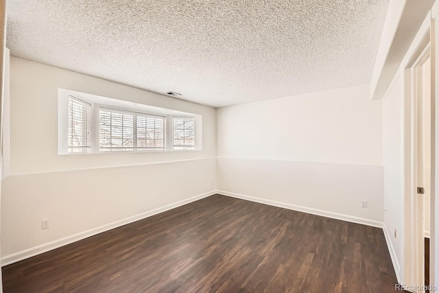 spare room featuring a textured ceiling and dark hardwood / wood-style flooring