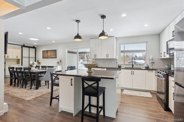 kitchen with sink, a breakfast bar, black gas stove, white cabinetry, and a kitchen island