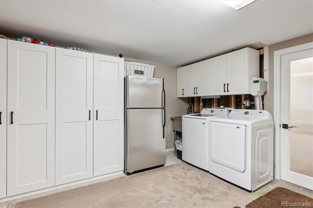 clothes washing area featuring separate washer and dryer, light colored carpet, and cabinets