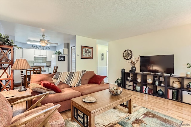 living room with ceiling fan, a textured ceiling, and light wood-type flooring