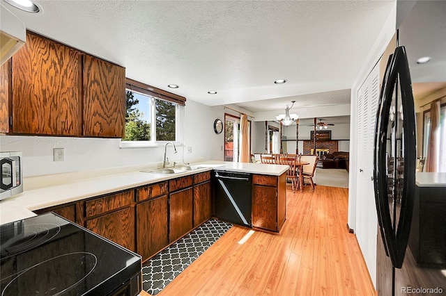 kitchen featuring a sink, light wood-style floors, light countertops, a peninsula, and black appliances