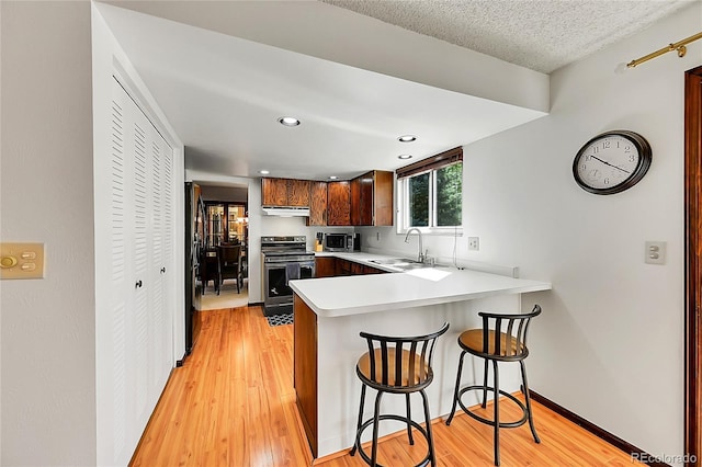 kitchen with a peninsula, light countertops, a sink, light wood-style flooring, and stainless steel appliances