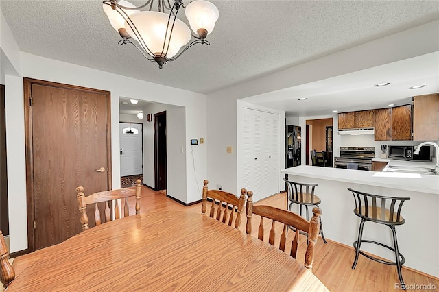 dining space featuring a textured ceiling, light wood-type flooring, baseboards, a notable chandelier, and recessed lighting