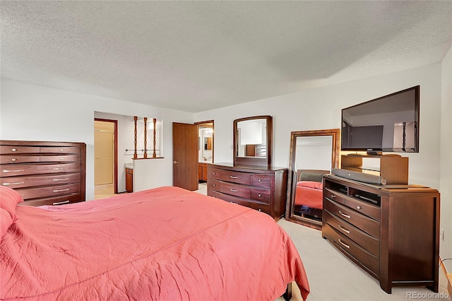 bedroom featuring light carpet, ensuite bath, and a textured ceiling