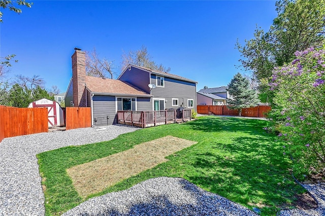 rear view of property featuring a wooden deck, a fenced backyard, a chimney, a storage unit, and an outbuilding