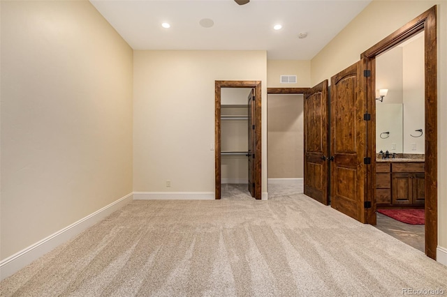 unfurnished bedroom featuring a closet, carpet, ensuite bathroom, sink, and a spacious closet