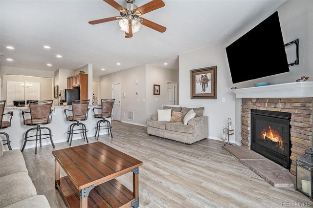 living room with a stone fireplace, light wood-type flooring, and ceiling fan