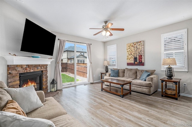 living room featuring a stone fireplace, light hardwood / wood-style flooring, and ceiling fan