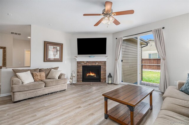 living room with ceiling fan, light wood-type flooring, and a stone fireplace