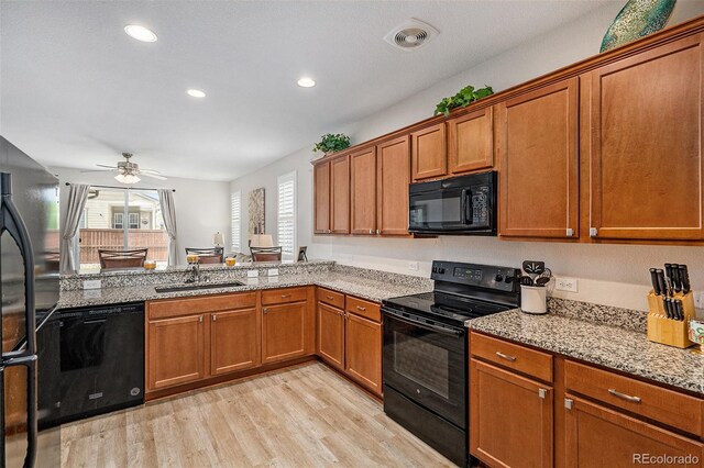 kitchen with light hardwood / wood-style flooring, ceiling fan, black appliances, light stone countertops, and sink