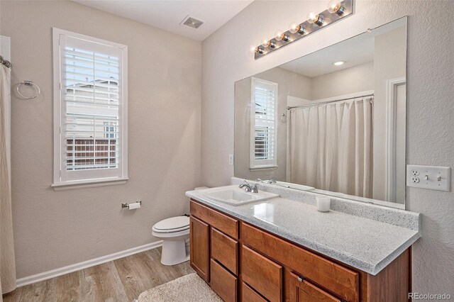 bathroom with wood-type flooring, vanity, a healthy amount of sunlight, and toilet