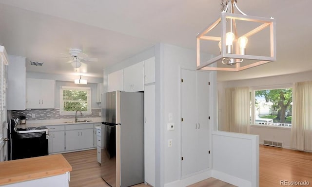 kitchen with stainless steel refrigerator, white cabinetry, sink, hanging light fixtures, and range