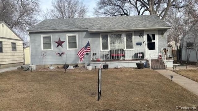 view of front of house with a front yard, a shingled roof, and covered porch