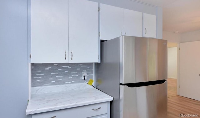 kitchen with tasteful backsplash, freestanding refrigerator, white cabinets, and light wood-style floors