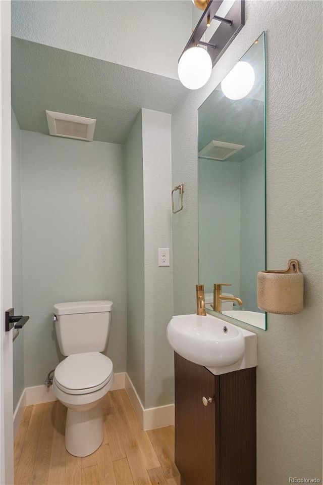 half bathroom featuring baseboards, wood finished floors, vanity, and toilet
