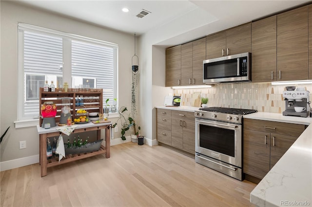kitchen with tasteful backsplash, stainless steel appliances, light wood-style flooring, baseboards, and visible vents