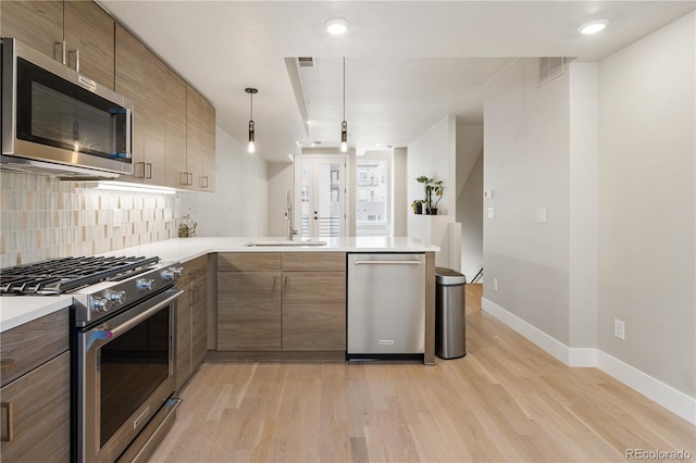 kitchen featuring stainless steel appliances, light wood-style flooring, a sink, backsplash, and light countertops