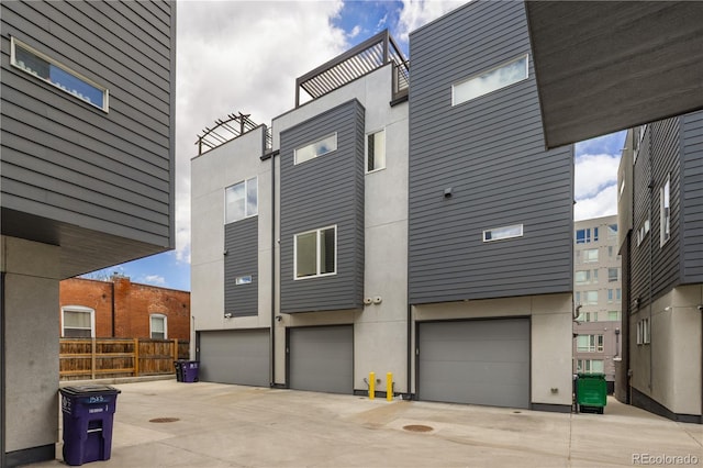 rear view of property with a garage, concrete driveway, stucco siding, and fence