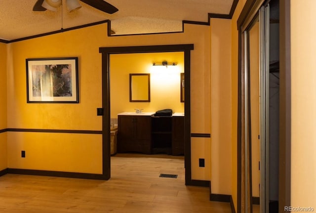 hall featuring a textured ceiling, crown molding, vaulted ceiling, and light wood-type flooring